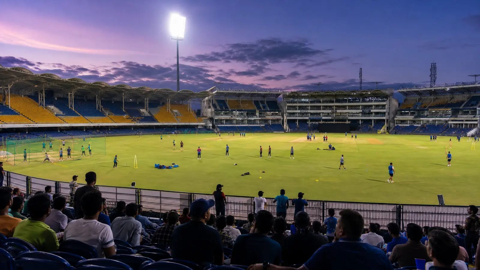 A floodlit cricket stadium with players warming up in the foreground